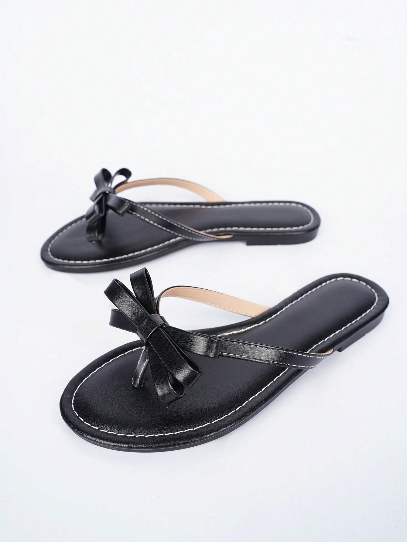 Women's flat slip-on slide sandals with textured PU leather look, bow detail on the upper, and toe-post design for casual vacation and beach wear.