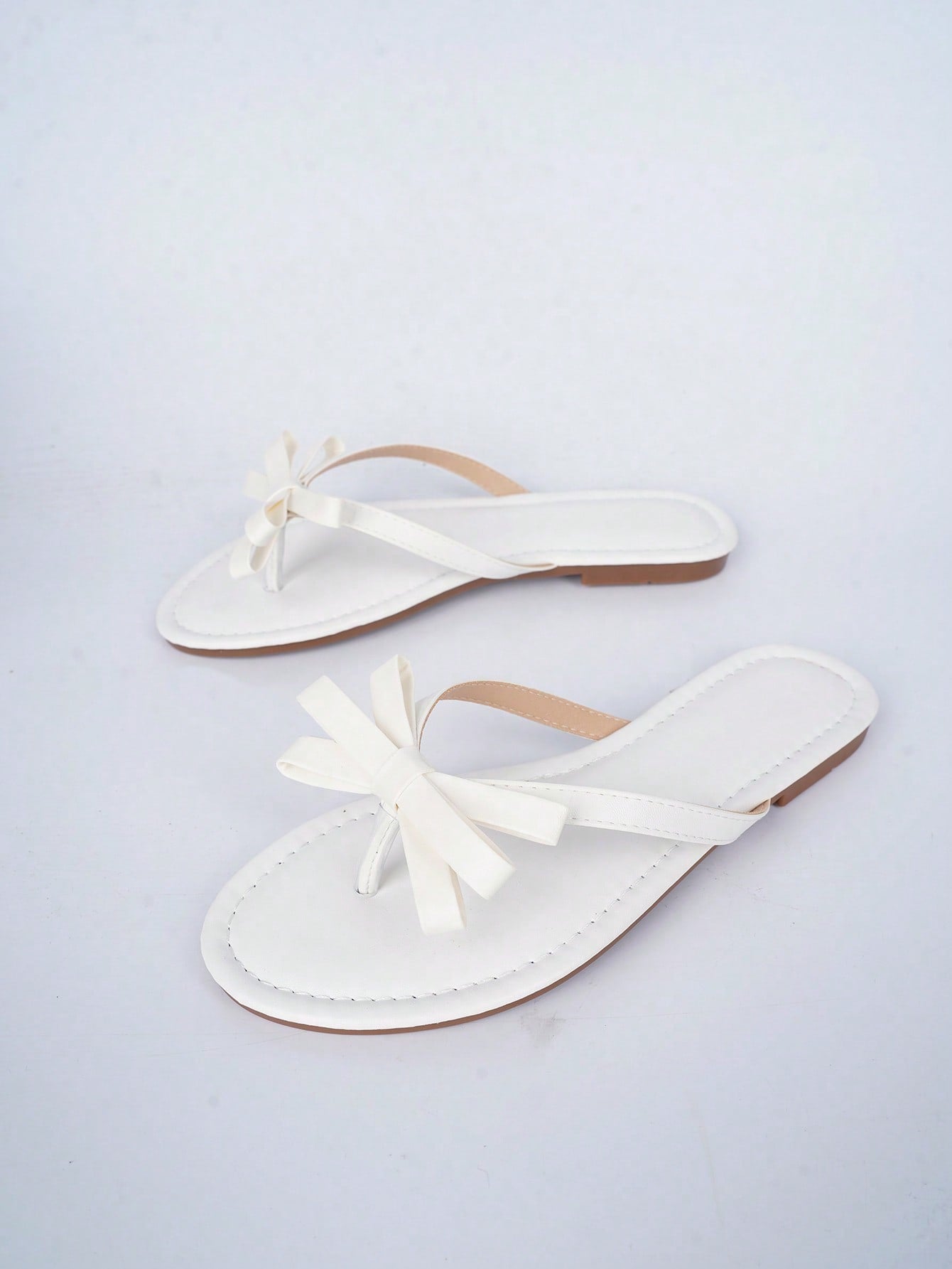 Women's flat slip-on slide sandals with textured PU leather look, bow detail on the upper, and toe-post design for casual vacation and beach wear.