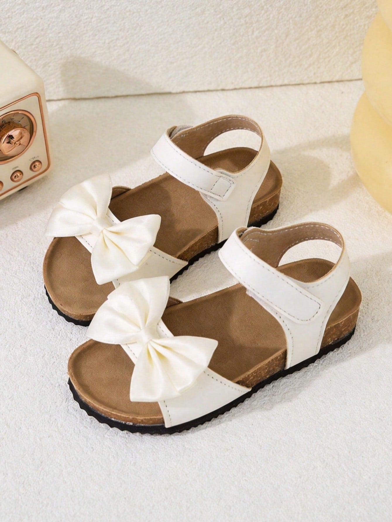 Pair of girls' pink open-toe flat sandals with ankle straps, buckle details, and a non-slip black rubber outsole.