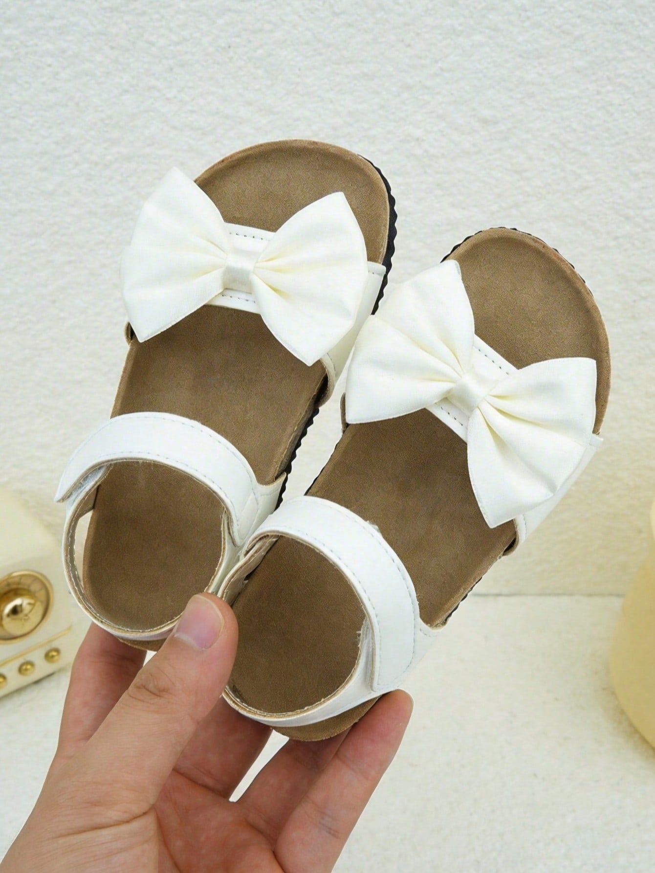 Pair of girls' pink open-toe flat sandals with ankle straps, buckle details, and a non-slip black rubber outsole.