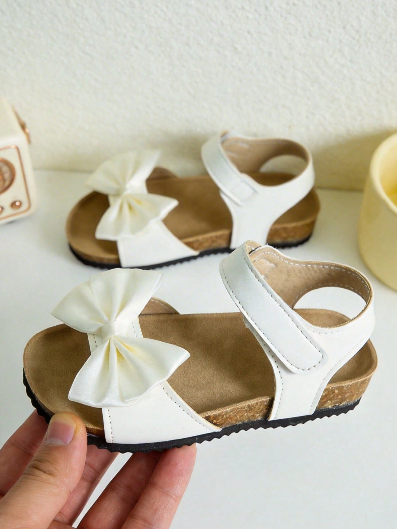Pair of girls' pink open-toe flat sandals with ankle straps, buckle details, and a non-slip black rubber outsole.