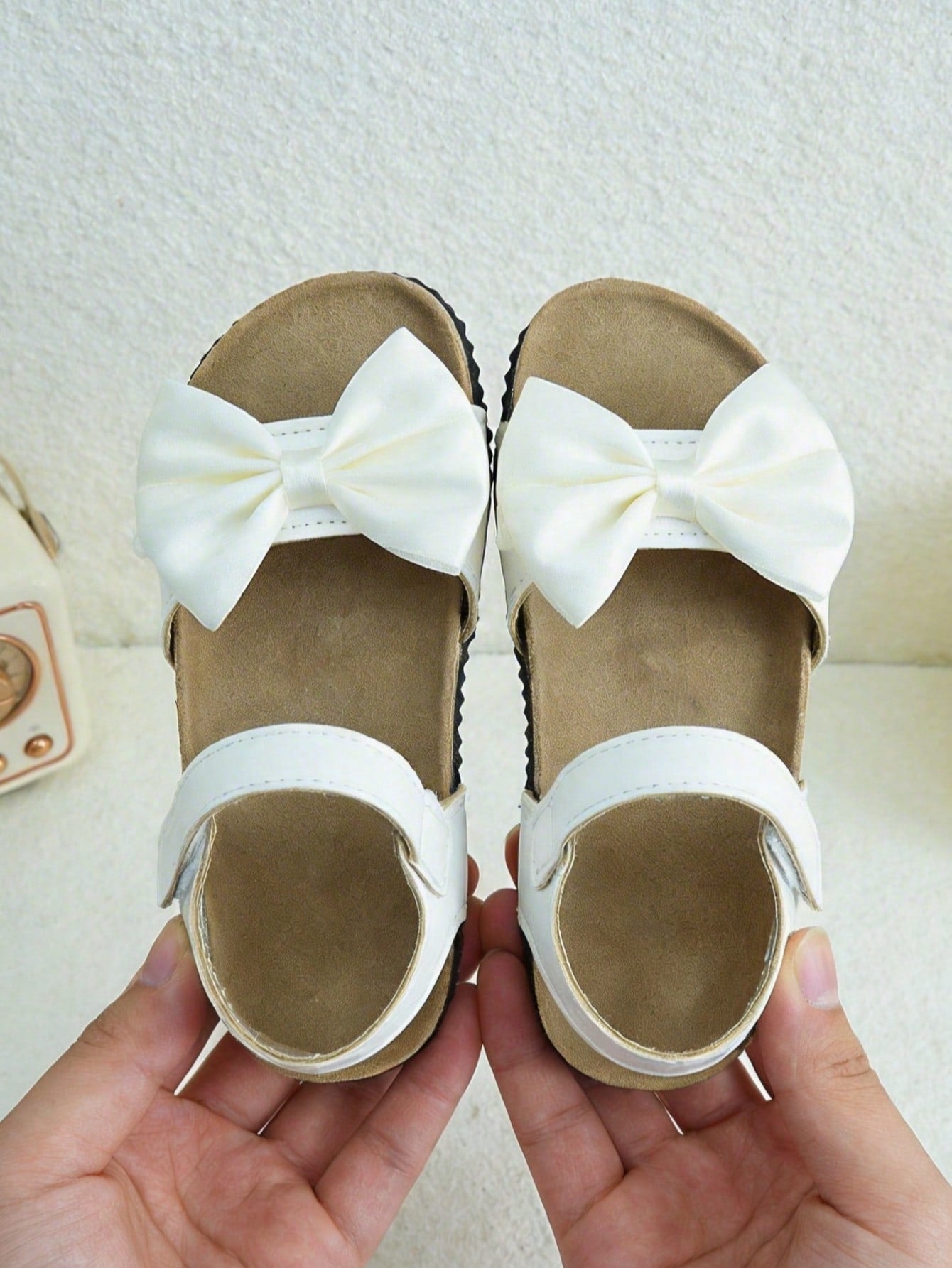 Pair of girls' pink open-toe flat sandals with ankle straps, buckle details, and a non-slip black rubber outsole.