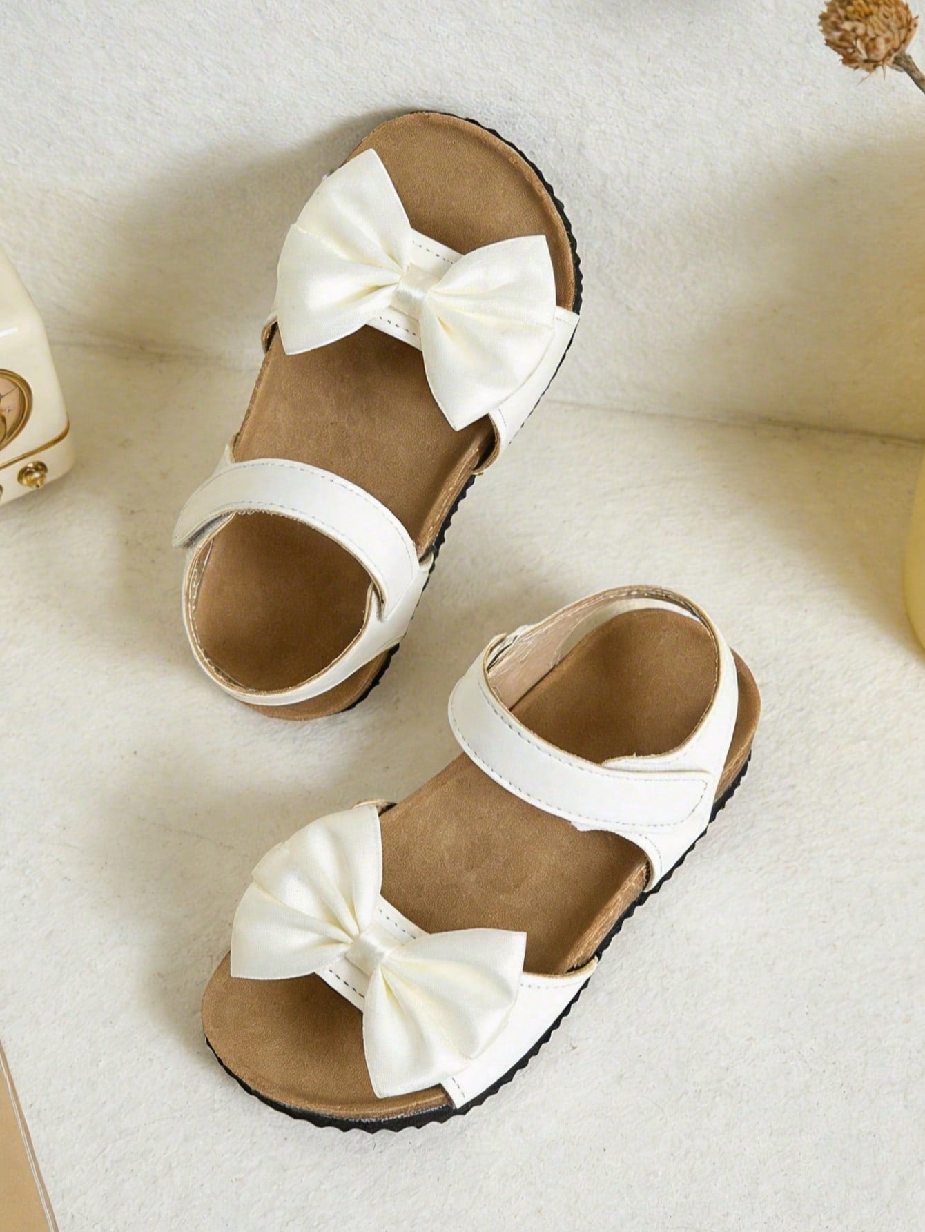 Pair of girls' pink open-toe flat sandals with ankle straps, buckle details, and a non-slip black rubber outsole.