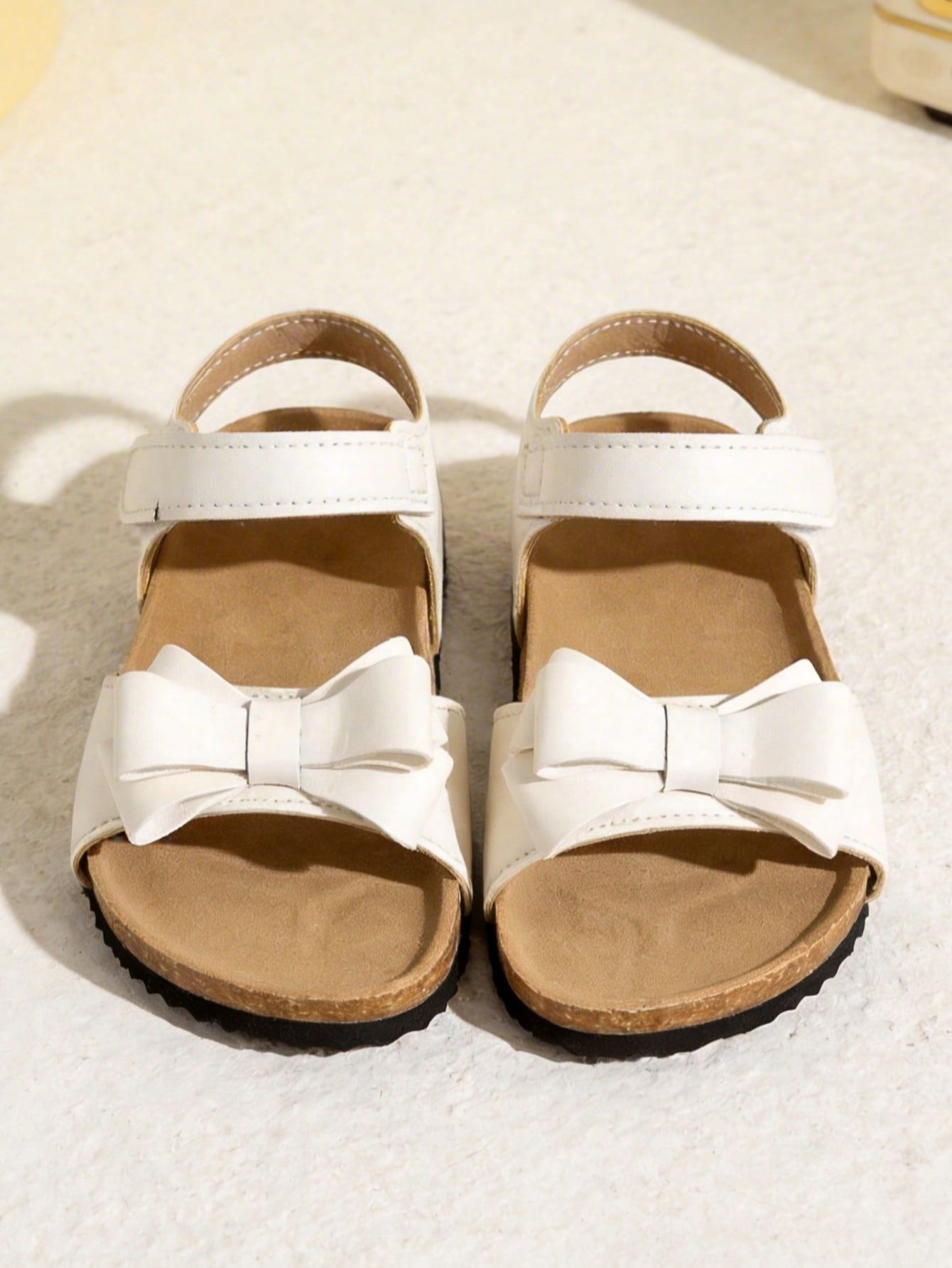 Pair of girls' pink open-toe flat sandals with ankle straps, buckle details, and a non-slip black rubber outsole.