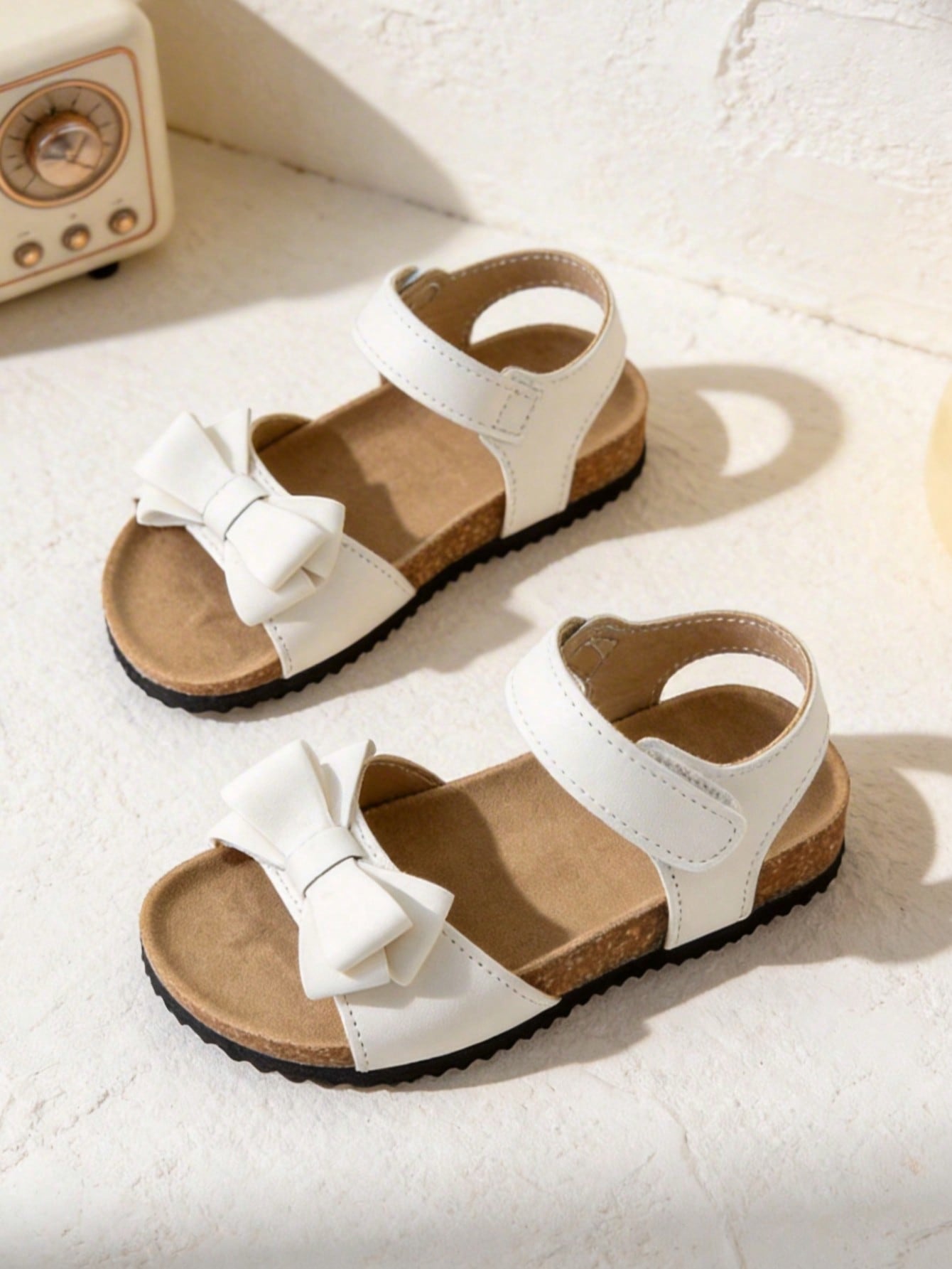 Pair of girls' pink open-toe flat sandals with ankle straps, buckle details, and a non-slip black rubber outsole.