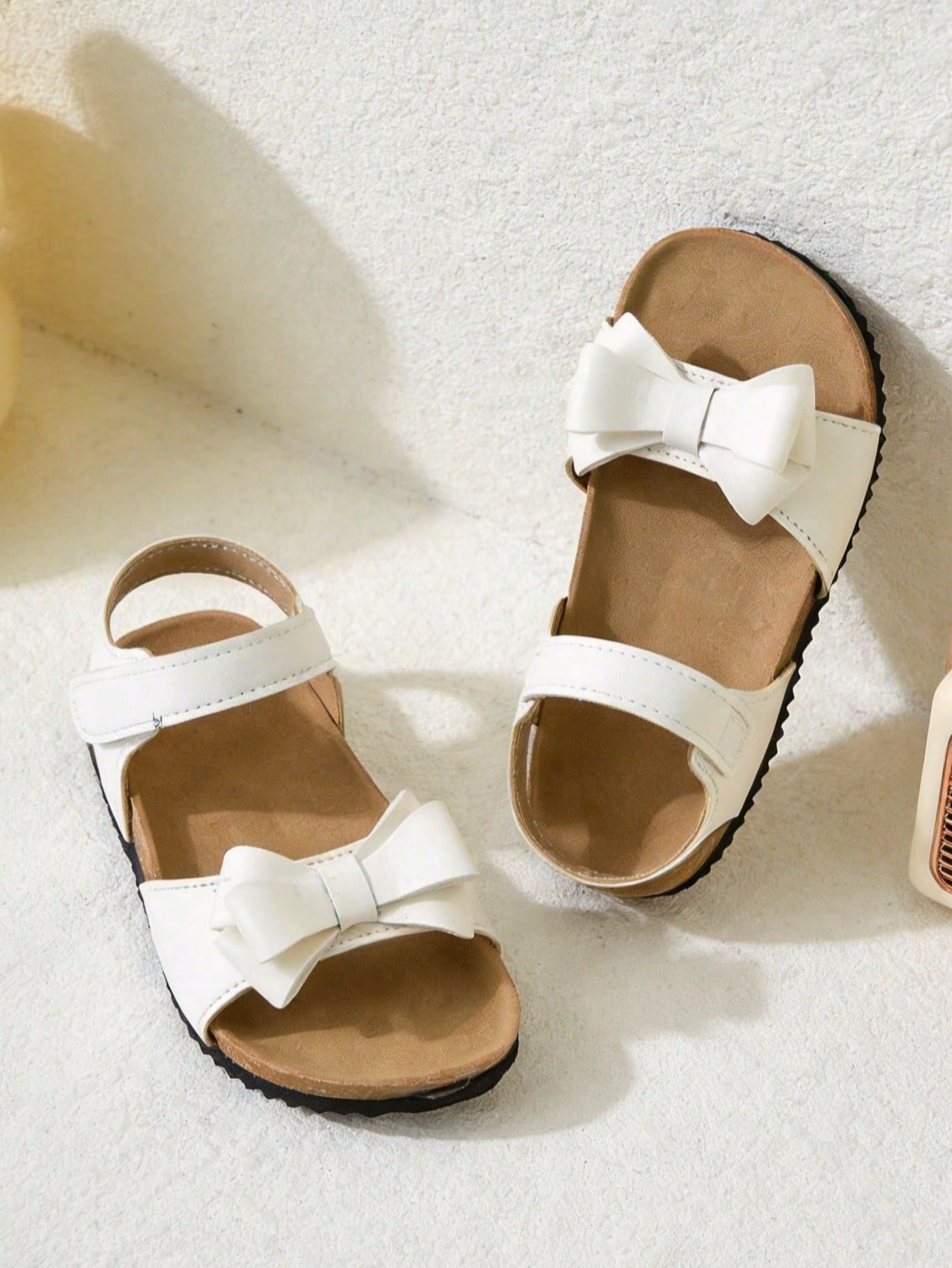 Pair of girls' pink open-toe flat sandals with ankle straps, buckle details, and a non-slip black rubber outsole.