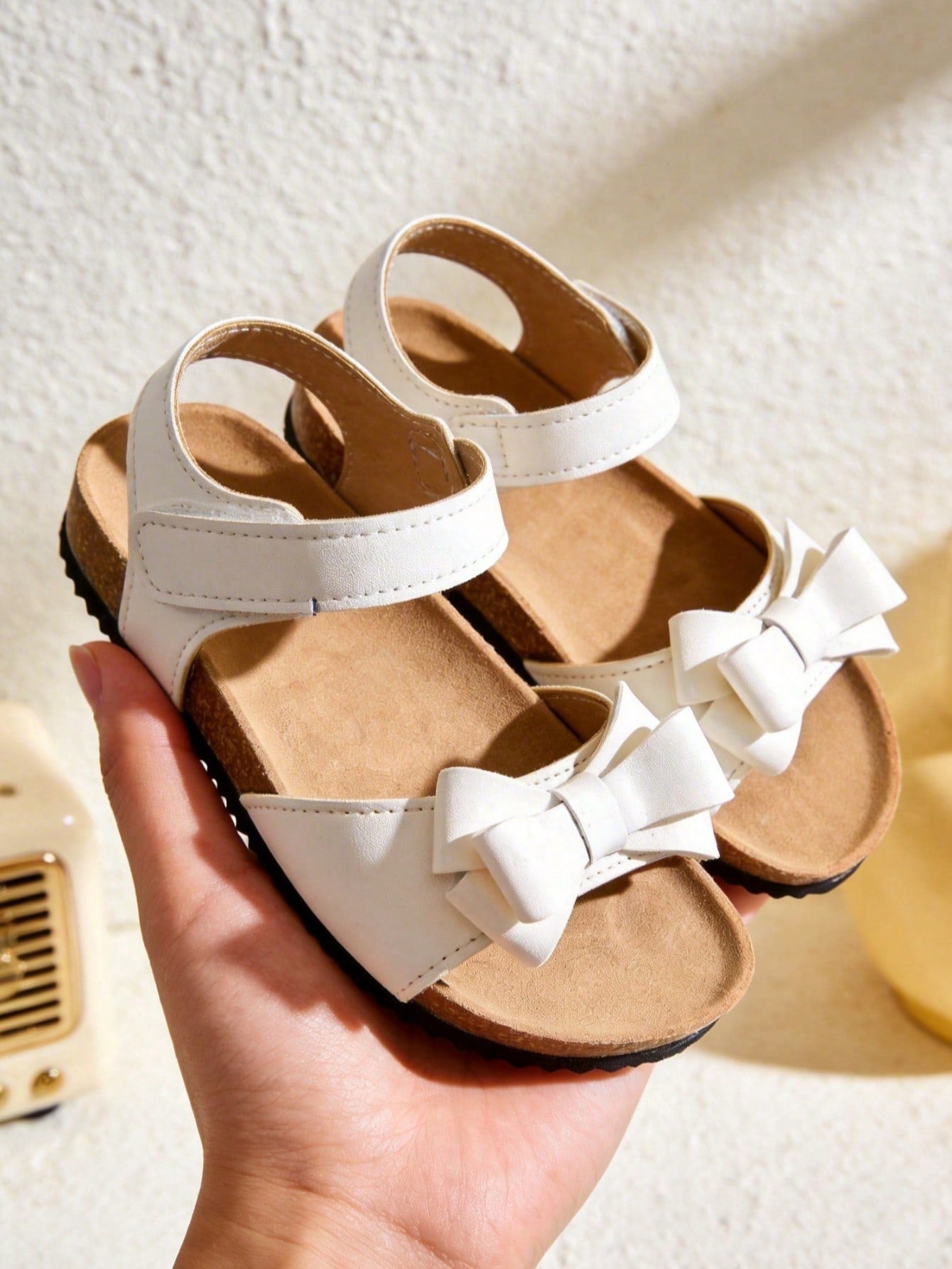 Pair of girls' pink open-toe flat sandals with ankle straps, buckle details, and a non-slip black rubber outsole.