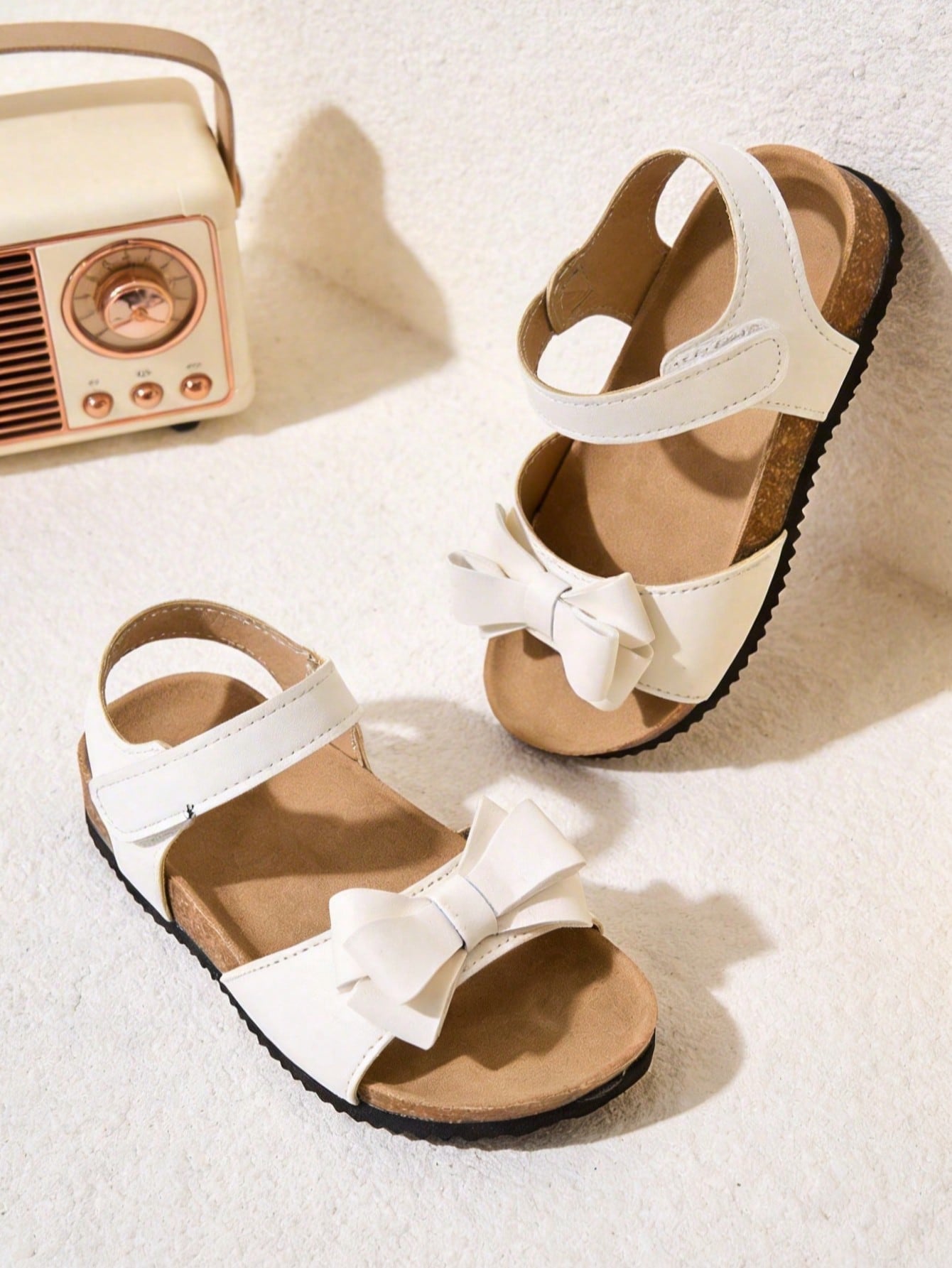 Pair of girls' pink open-toe flat sandals with ankle straps, buckle details, and a non-slip black rubber outsole.