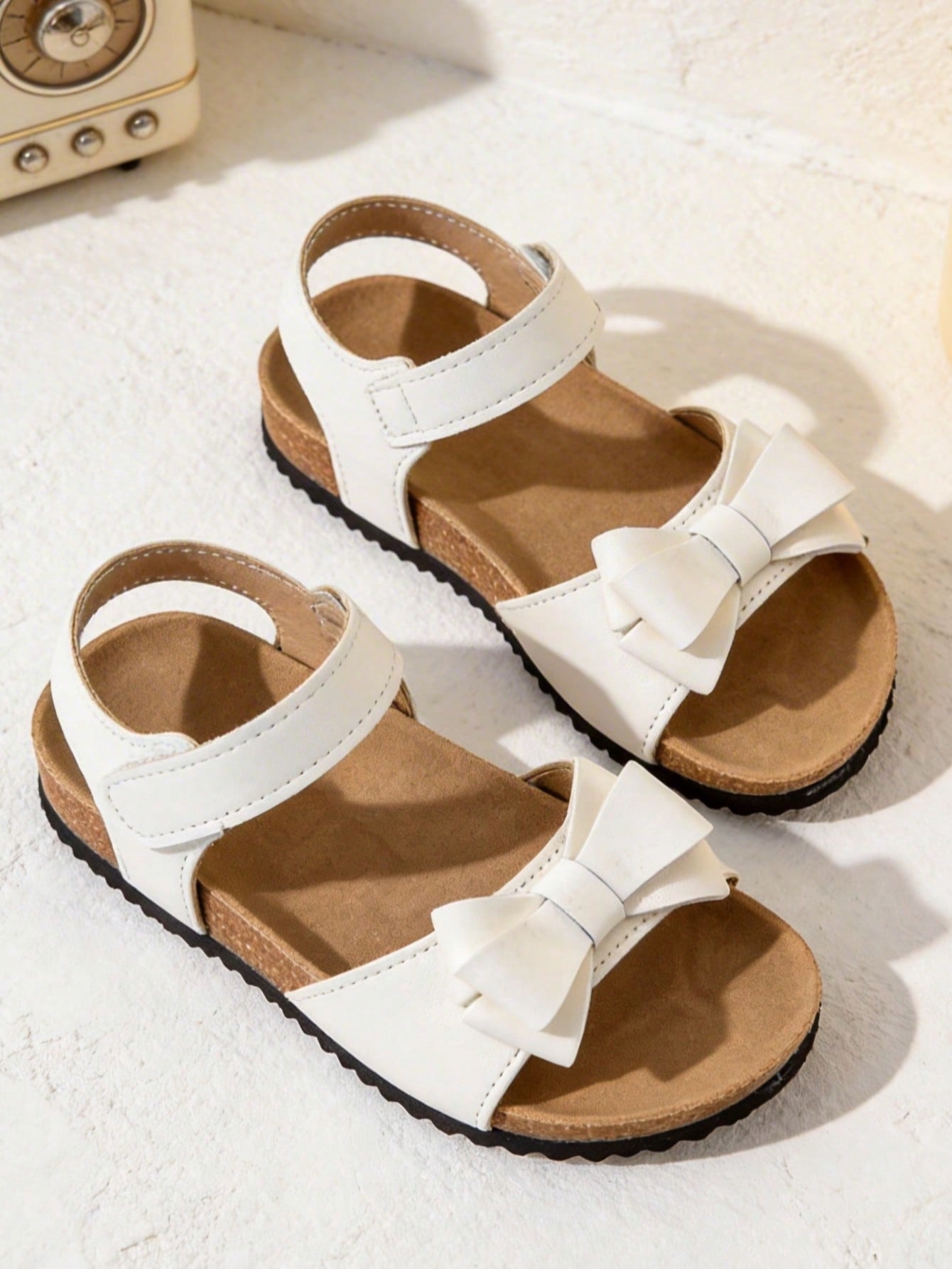 Pair of girls' pink open-toe flat sandals with ankle straps, buckle details, and a non-slip black rubber outsole.