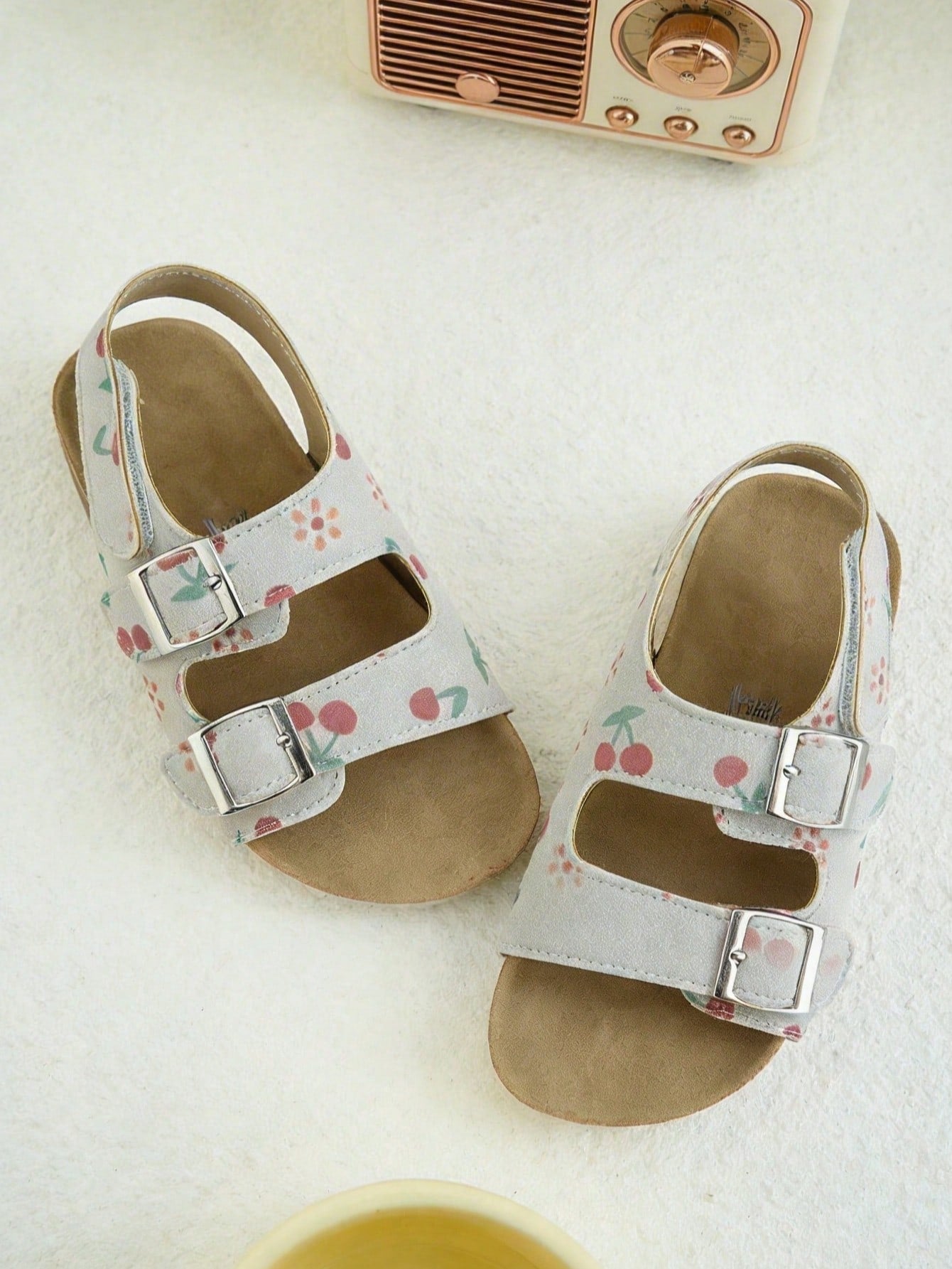 Pair of girls' pink open-toe flat sandals with ankle straps, buckle details, and a non-slip black rubber outsole.