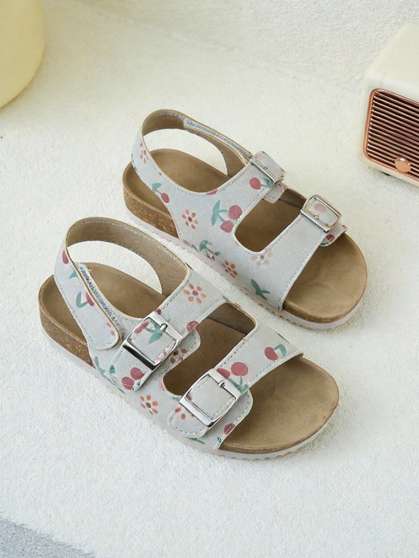 Pair of girls' pink open-toe flat sandals with ankle straps, buckle details, and a non-slip black rubber outsole.