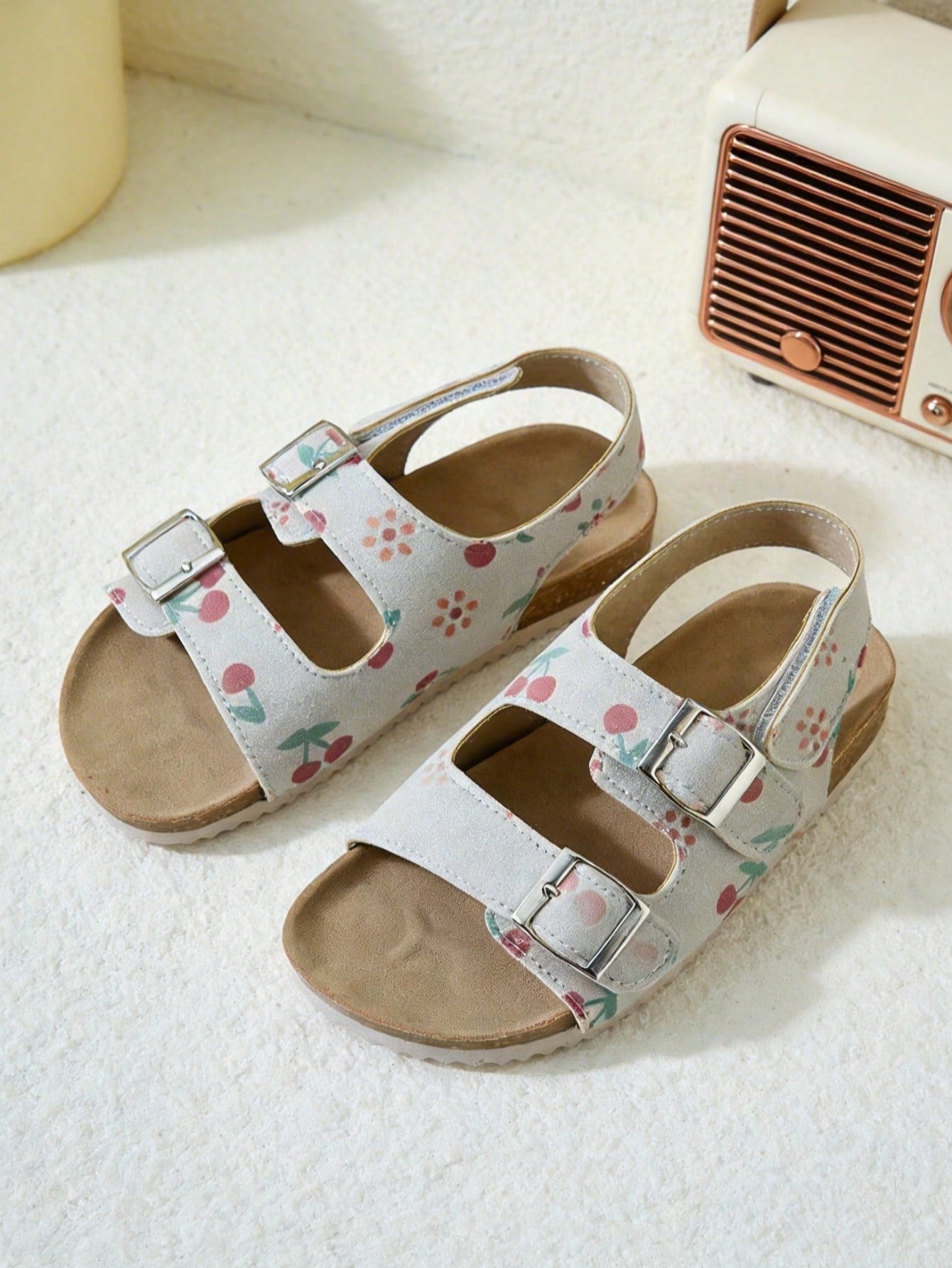 Pair of girls' pink open-toe flat sandals with ankle straps, buckle details, and a non-slip black rubber outsole.