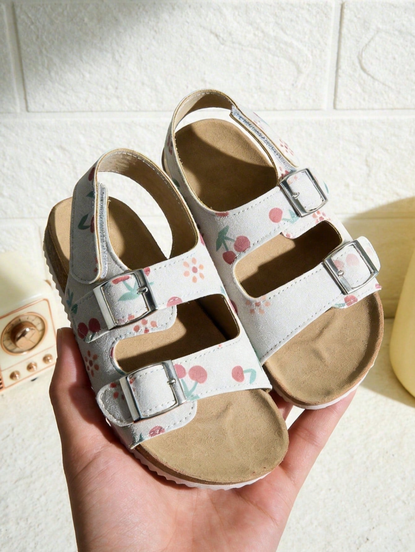 Pair of girls' pink open-toe flat sandals with ankle straps, buckle details, and a non-slip black rubber outsole.