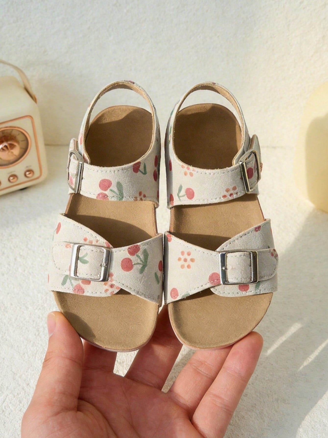 Pair of girls' pink open-toe flat sandals with ankle straps, buckle details, and a non-slip black rubber outsole.