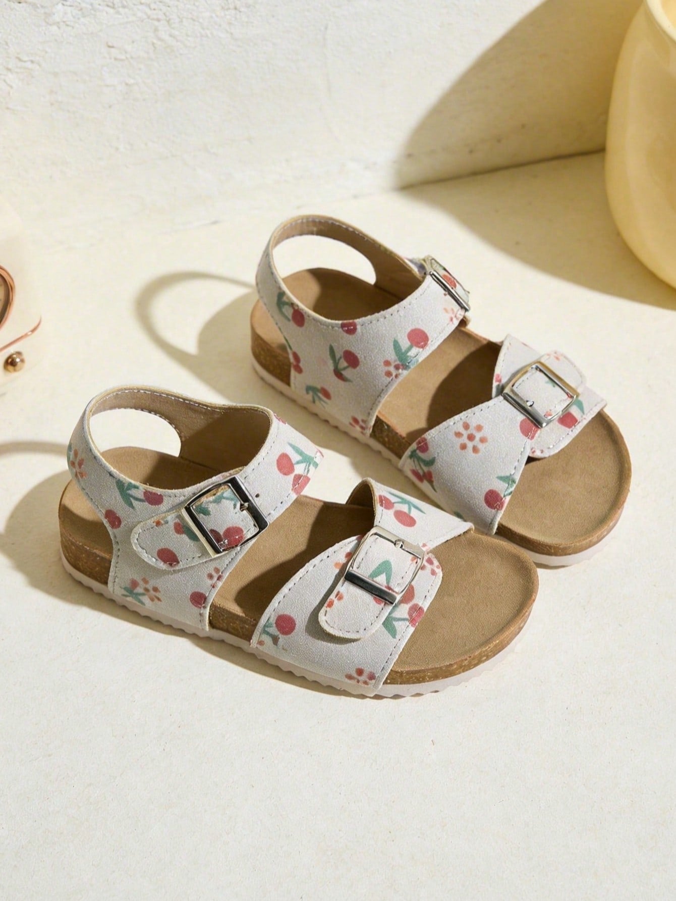 Pair of girls' pink open-toe flat sandals with ankle straps, buckle details, and a non-slip black rubber outsole.