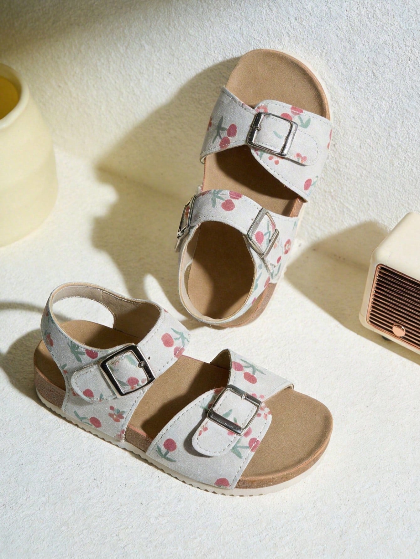 Pair of girls' pink open-toe flat sandals with ankle straps, buckle details, and a non-slip black rubber outsole.