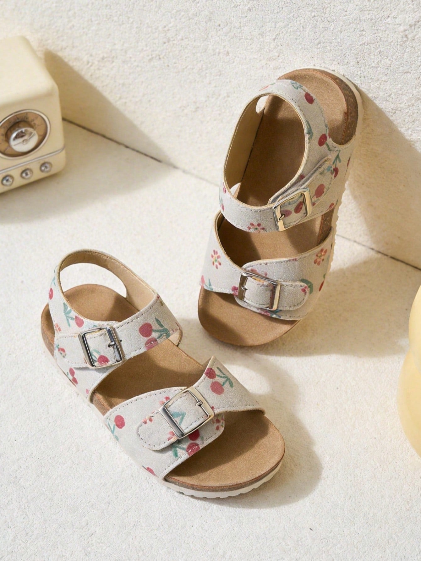 Pair of girls' pink open-toe flat sandals with ankle straps, buckle details, and a non-slip black rubber outsole.