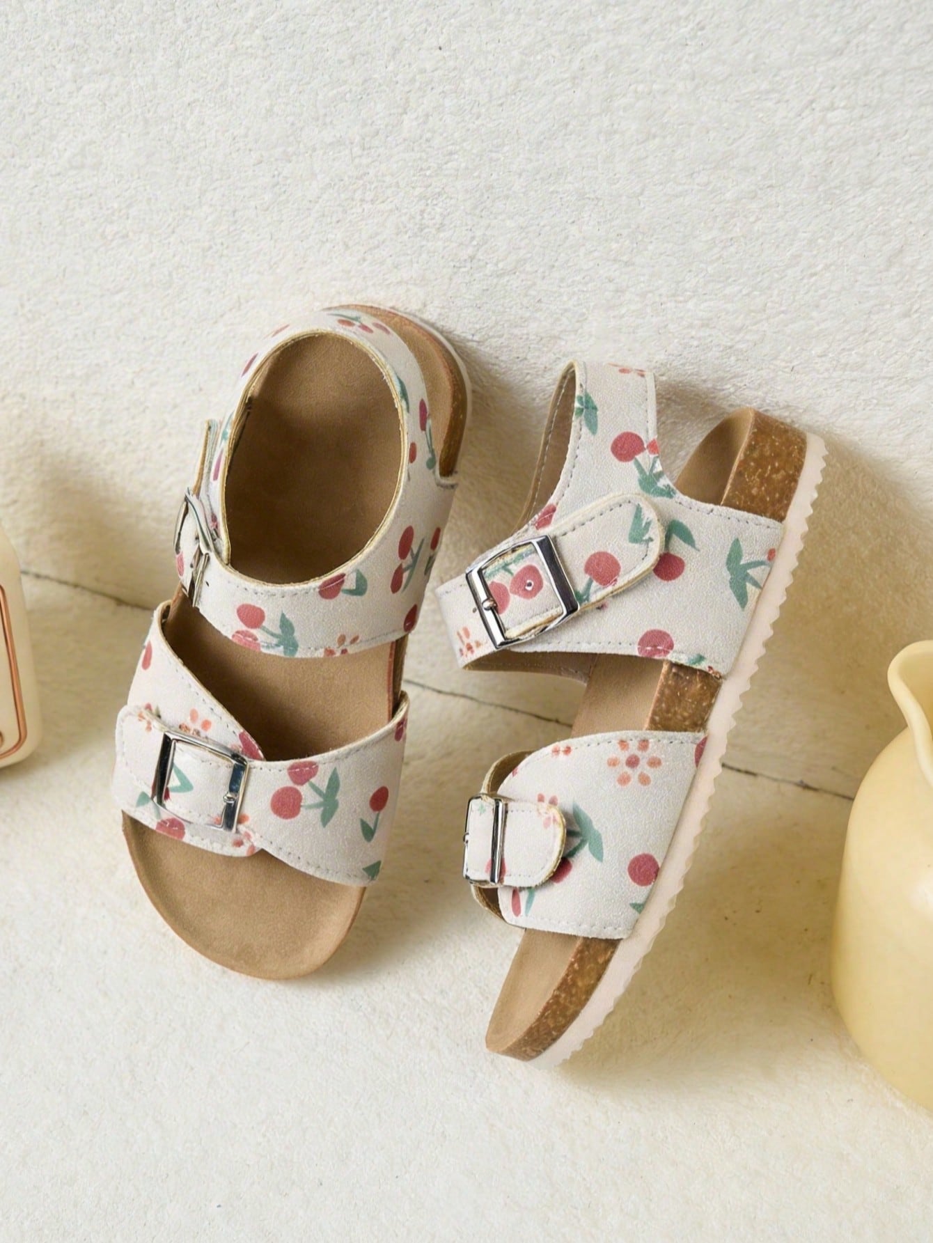 Pair of girls' pink open-toe flat sandals with ankle straps, buckle details, and a non-slip black rubber outsole.
