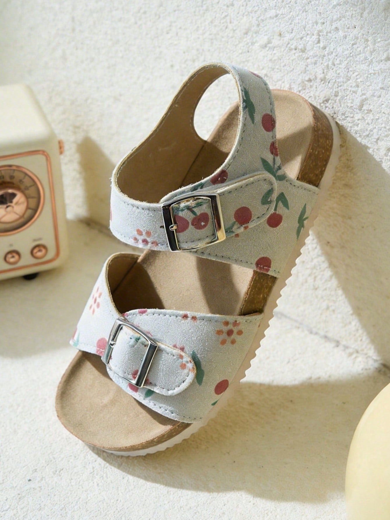 Pair of girls' pink open-toe flat sandals with ankle straps, buckle details, and a non-slip black rubber outsole.