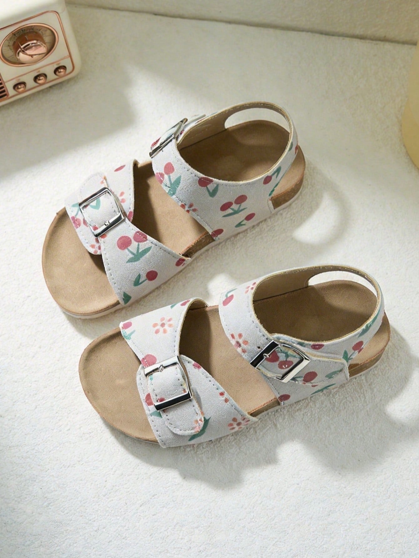 Pair of girls' pink open-toe flat sandals with ankle straps, buckle details, and a non-slip black rubber outsole.