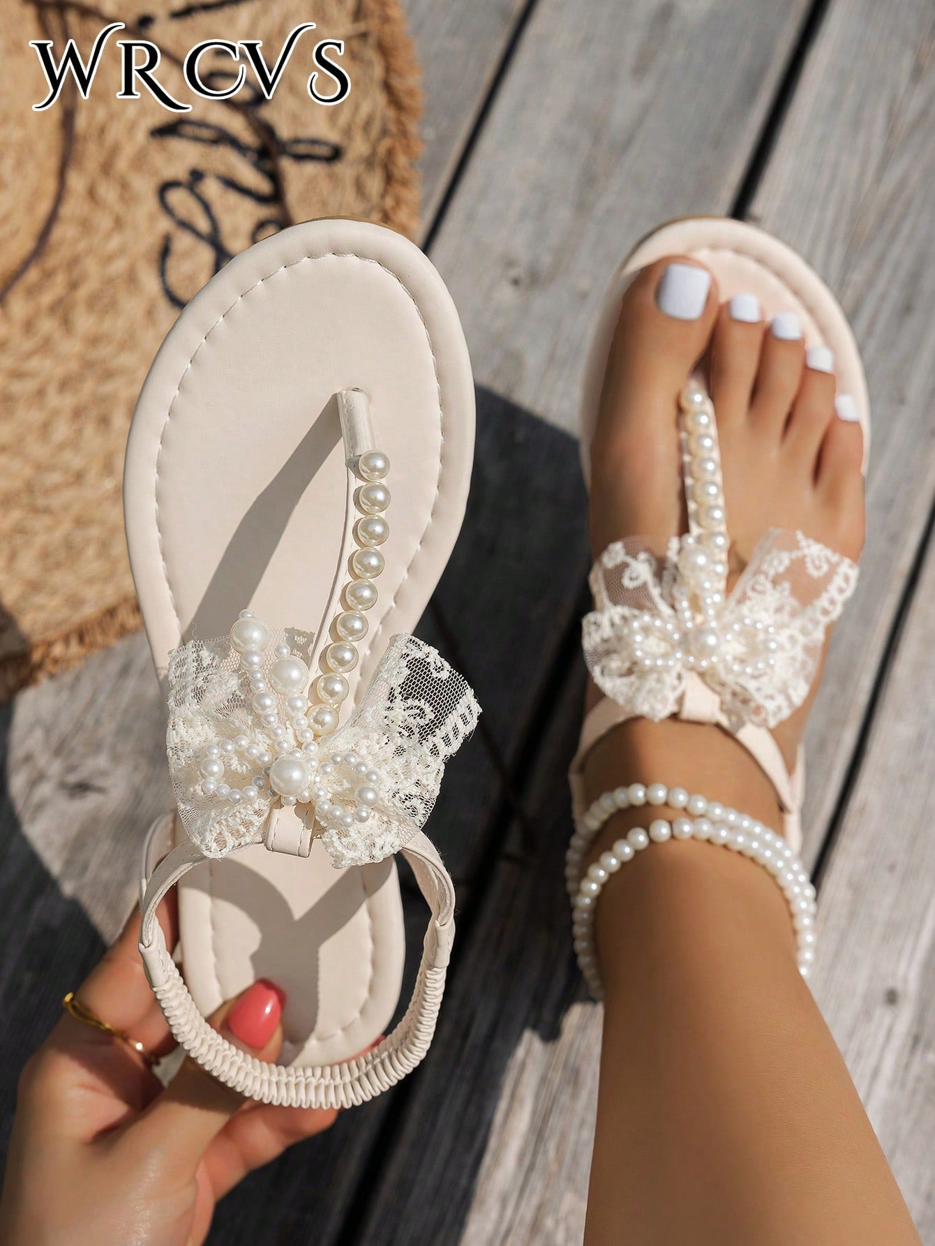 Beige women's flat thong Roman-style sandals with toe post, rhinestone and bow decoration, and buckle detail.