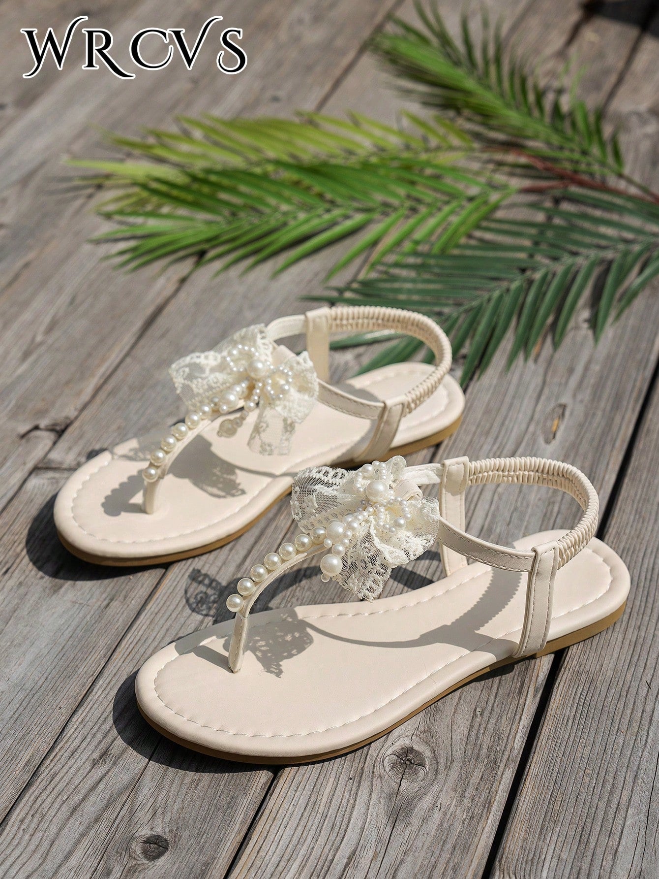 Beige women's flat thong Roman-style sandals with toe post, rhinestone and bow decoration, and buckle detail.