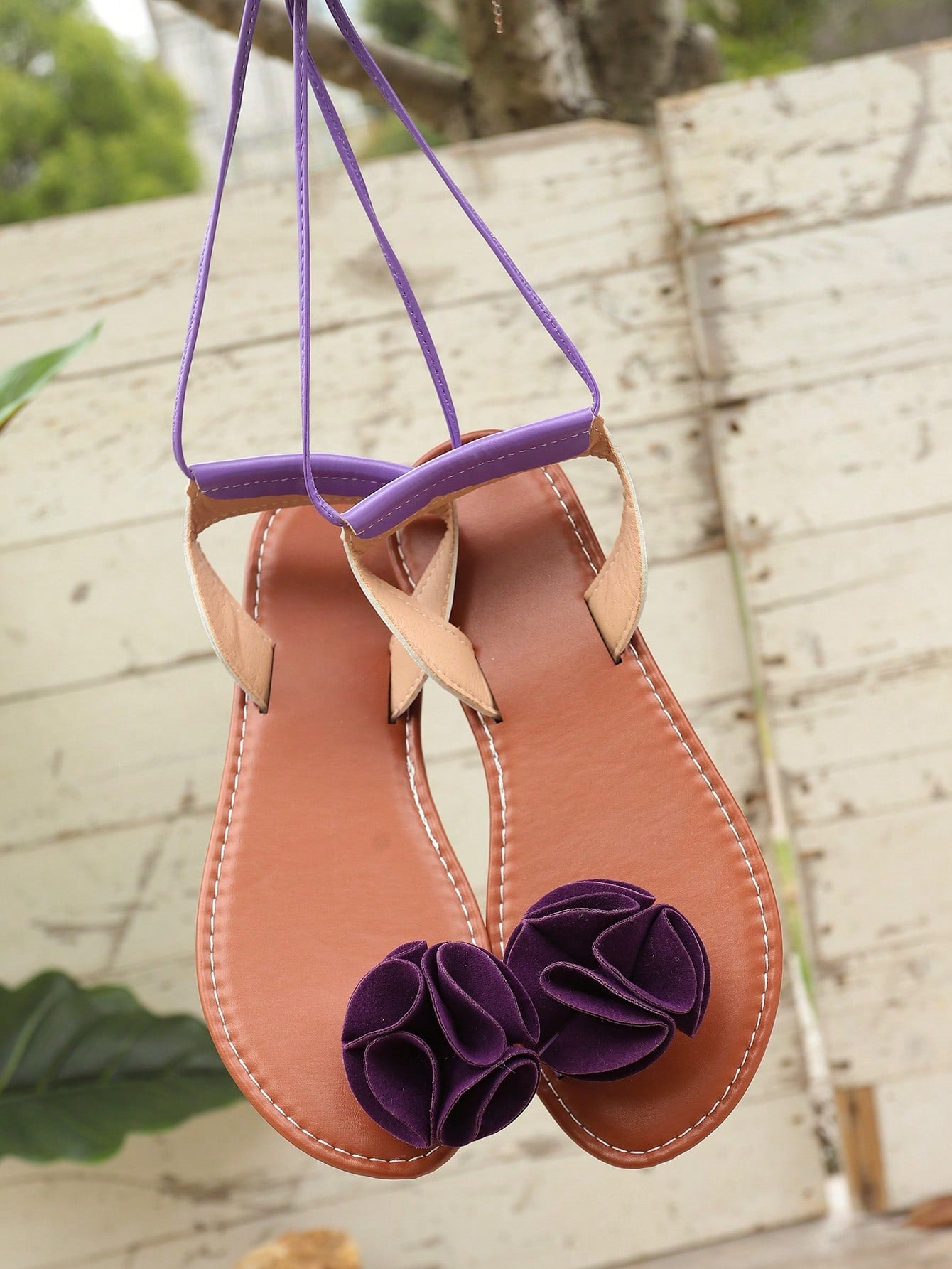 Women's flat strappy toe-post sandals with floral camellia-style appliques and ankle lace-up detail, elegant beach and holiday style, available in white, green, purple, and black.