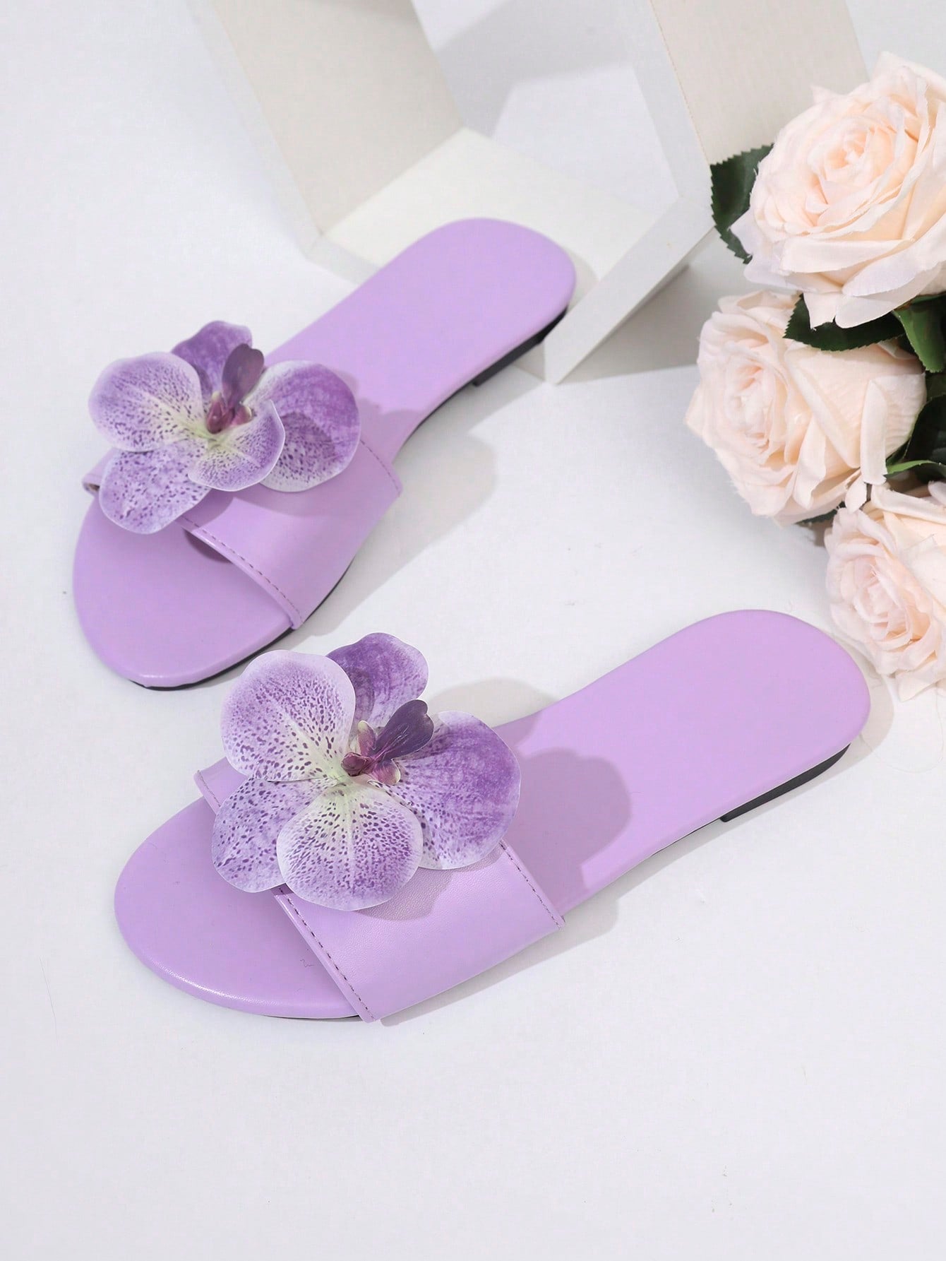 Women’s open toe flat toe-ring slide sandals with artificial flower applique detail and vacation beach style.