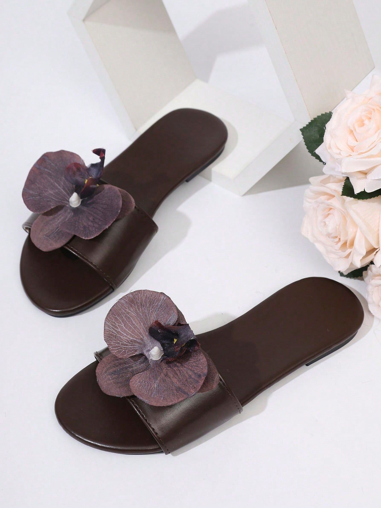 Women’s open toe flat toe-ring slide sandals with artificial flower applique detail and vacation beach style.