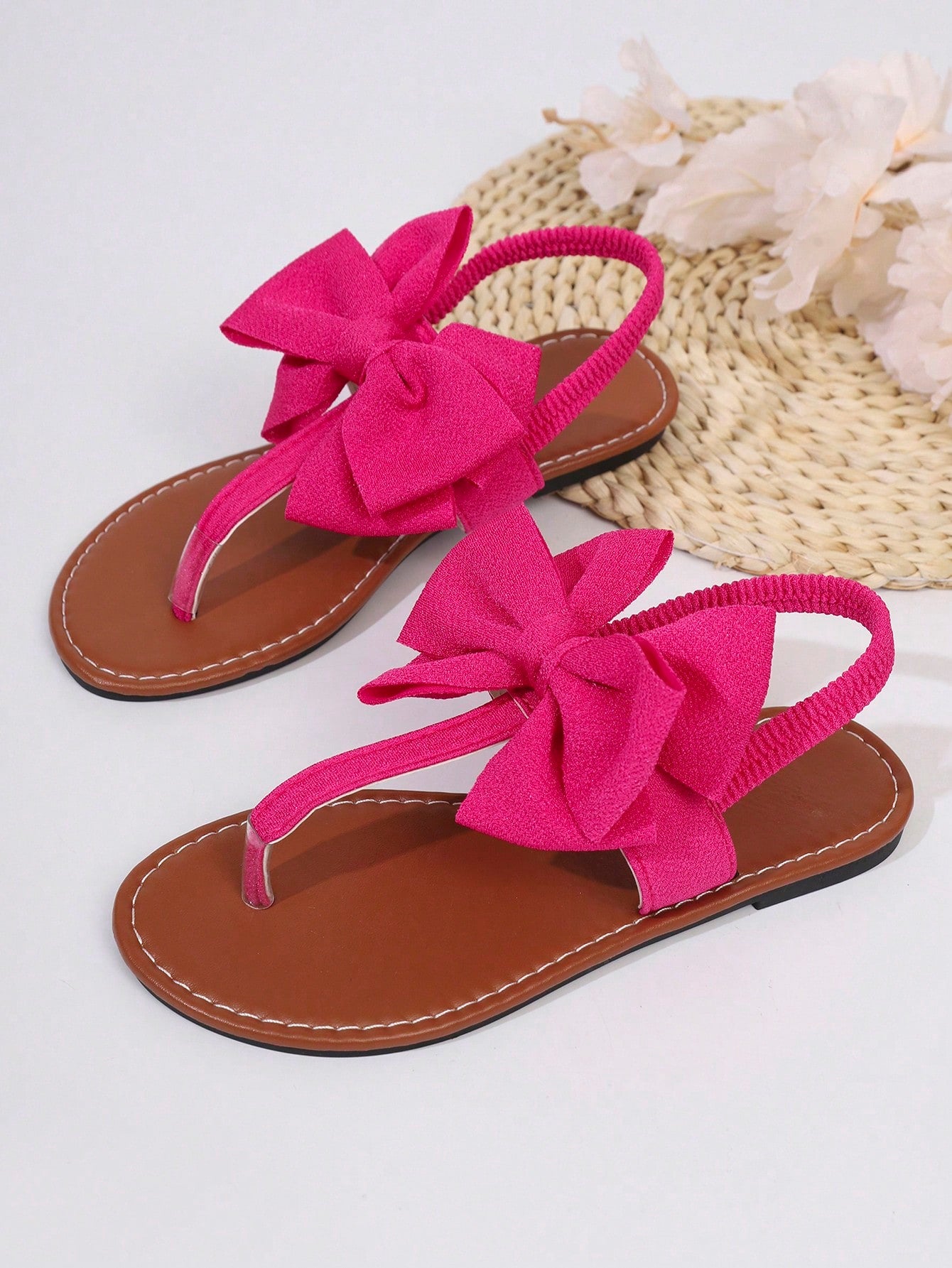Pair of women’s solid color bohemian flat sandals with fabric bow detail, toe post thong design, and slide-on style for casual beach, outdoor, vacation, and home wear.