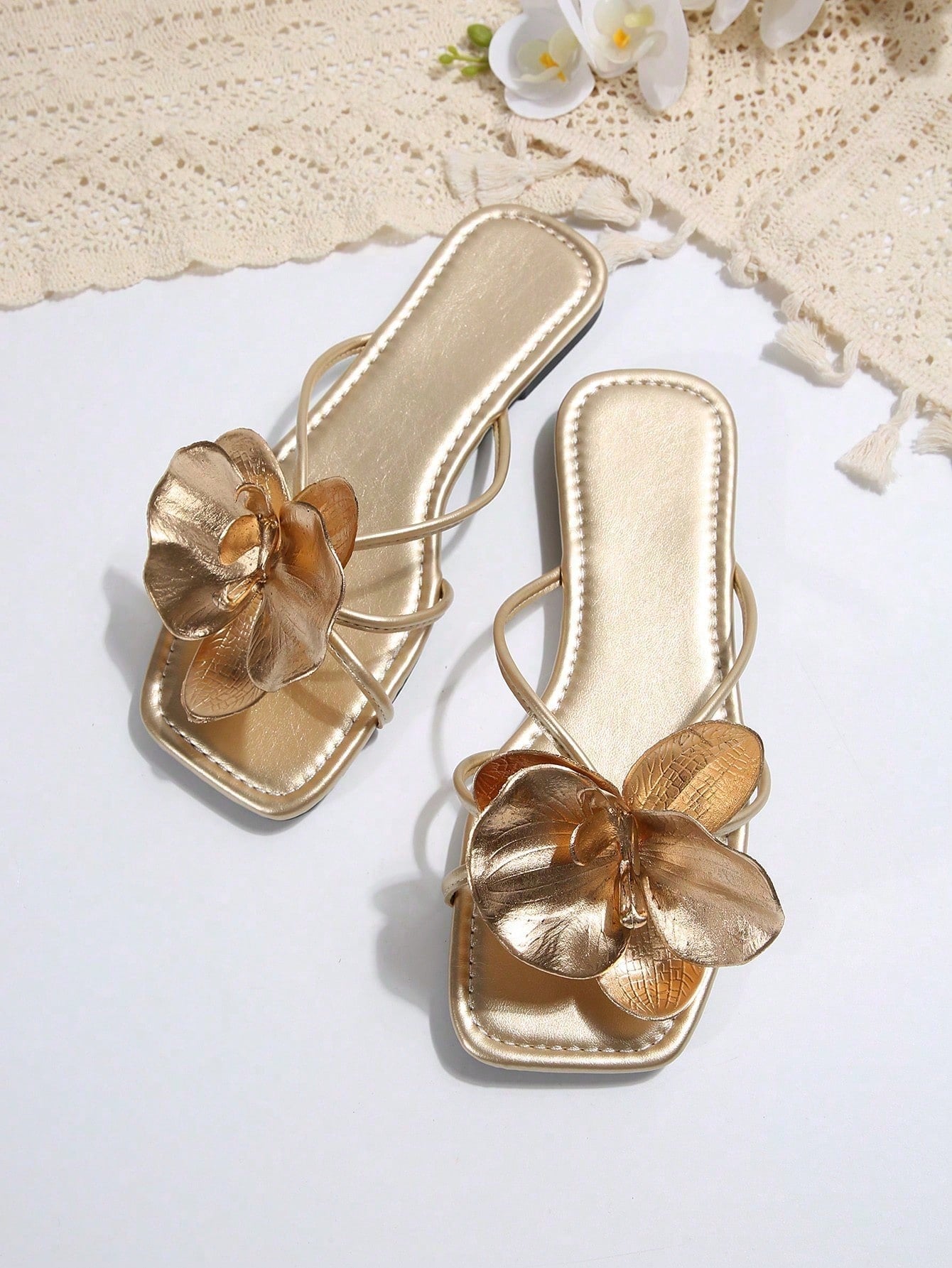Women's flat slide sandals with open toe, floral applique detail, and criss-cross straps, shown as casual vacation-style summer footwear.