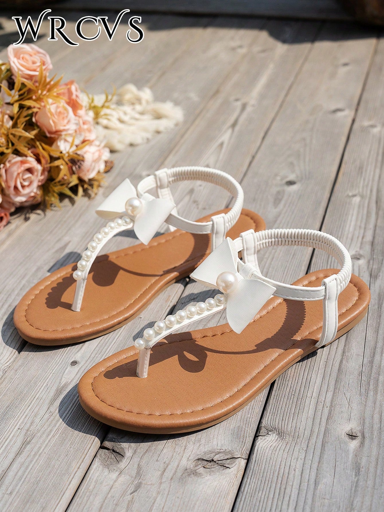 Beige women's flat thong Roman-style sandals with toe post, rhinestone and bow decoration, and buckle detail.
