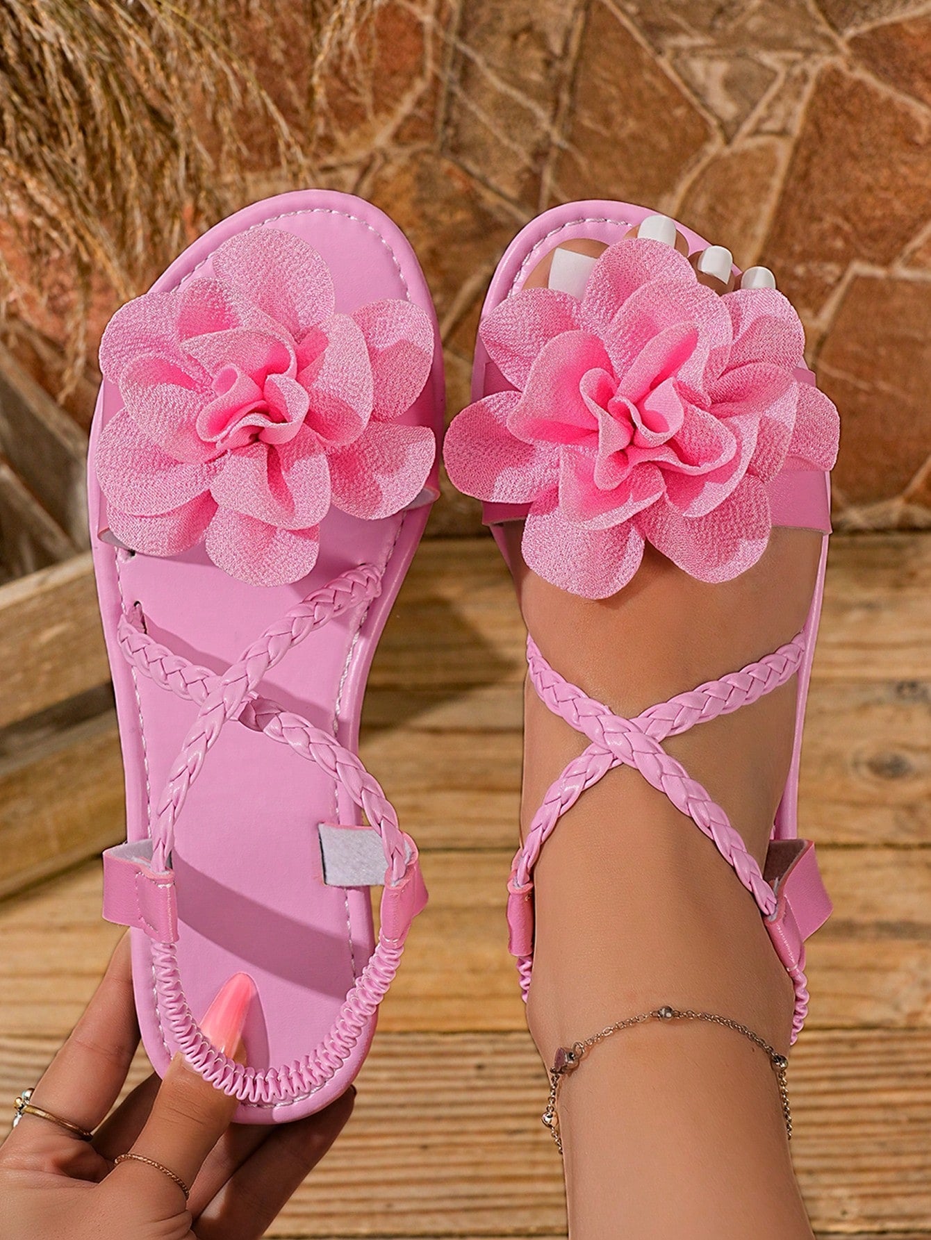 Women's open-toe flat slide sandals with crossed woven-look straps, floral appliqué detail, and buckle accent, shown in a casual beach style.