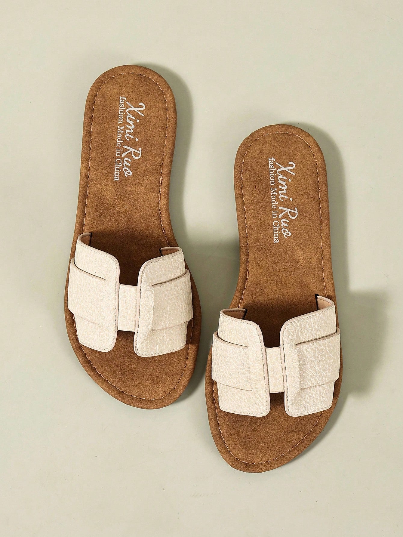 Pair of women’s open-toe flat slide sandals with an H-shaped strap, braided and embossed details, and a minimalist slip-on design suitable for casual outdoor wear.