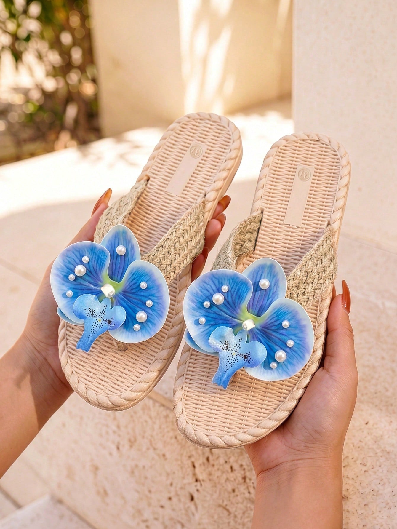 Women's flat woven slide sandals with open toe, featuring 3D flower and pearl appliques in an apricot and blue flower colorway, shown as casual vacation beach slippers.