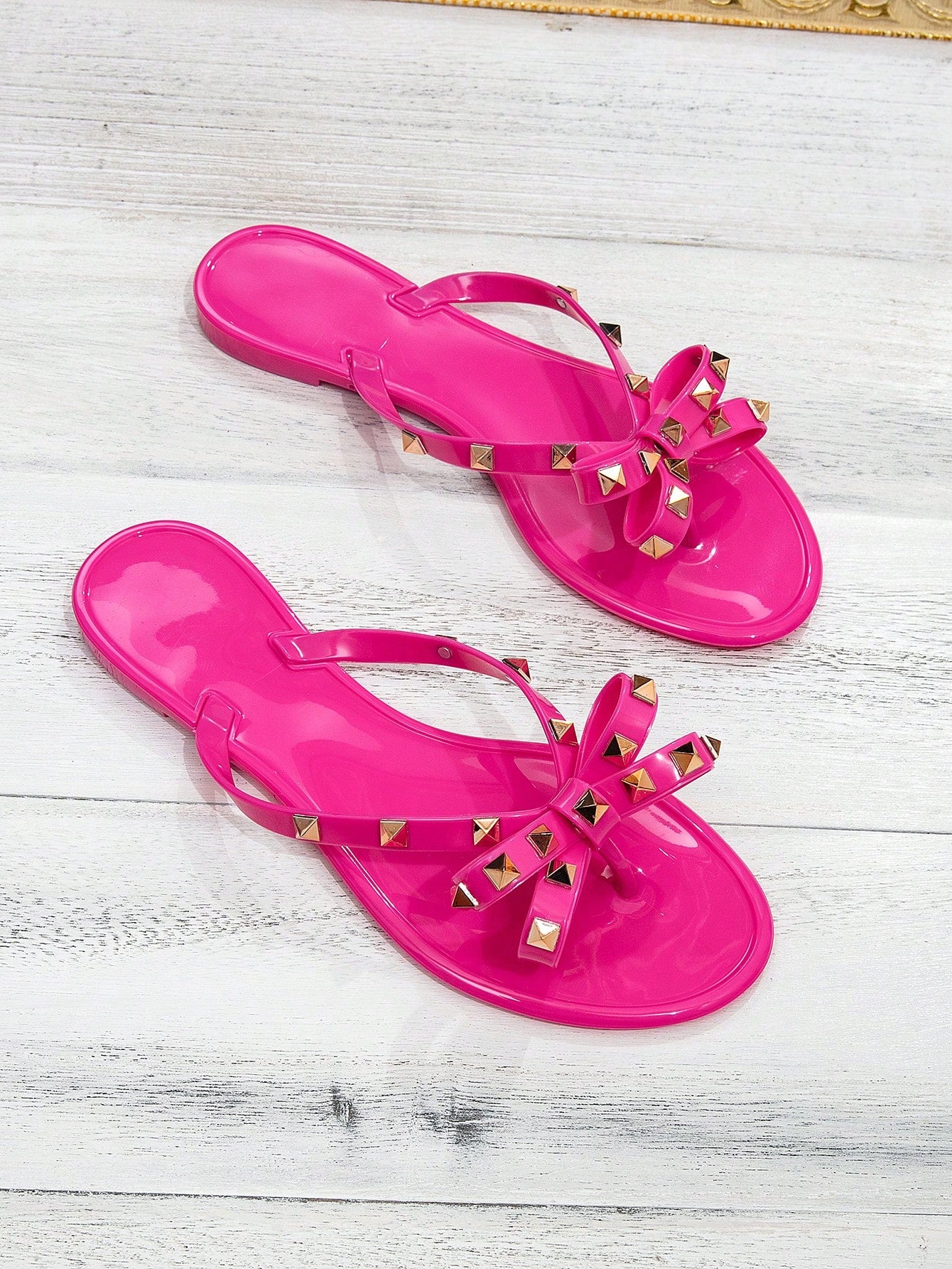 Pair of women's flat thong flip-flop sandals featuring bow decor and square stud accents, suitable for summer beach, resort, vacation, and everyday wear.
