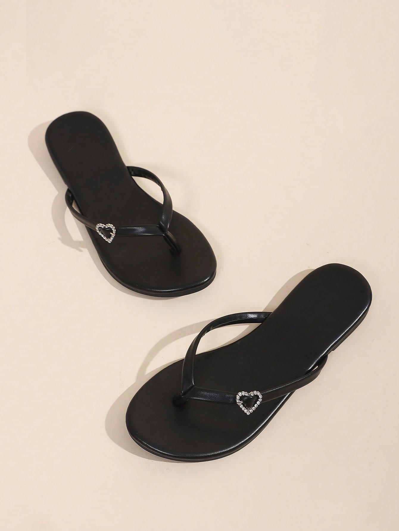Women's black flat slide sandals with toe post design, textured PU leather straps, and rhinestone heart decoration.