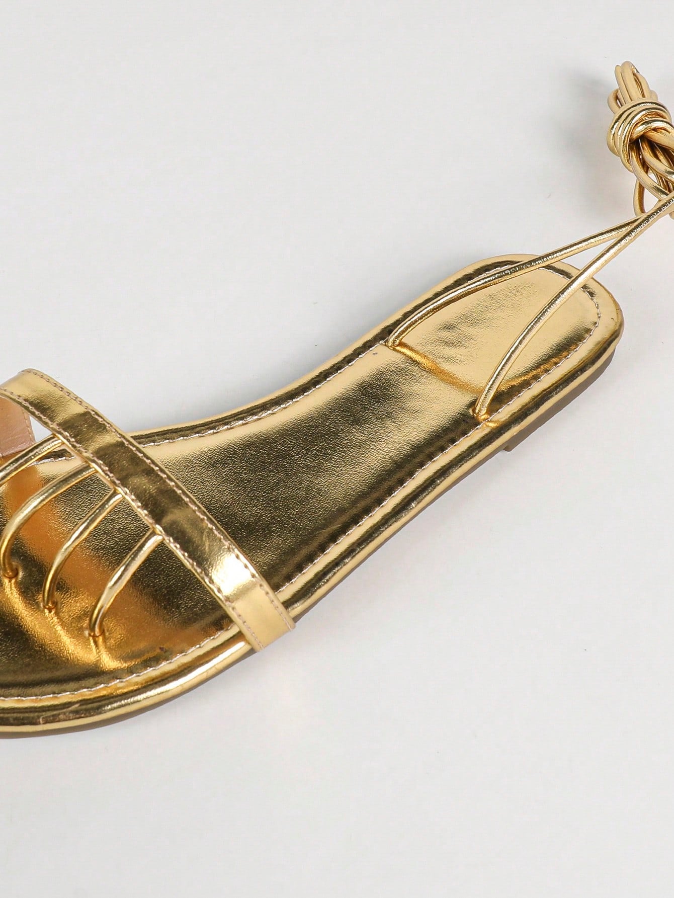 Women's gold flat sandals with metal accent detail, strappy lace-up design, and toe post thong style.